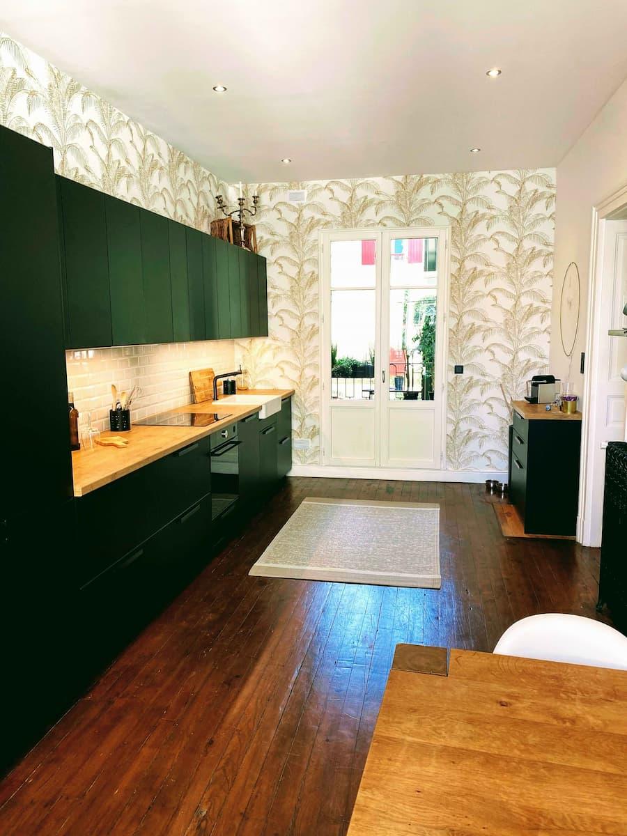 The black kitchen, with wooden worktop and leaf-pattern wallpaper